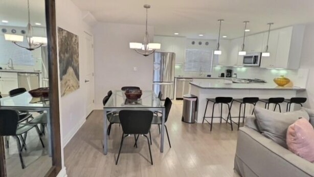 A modern kitchen with a central island, bar stools, and a dining area with a glass table and chairs. - Frank's Pismo Beach House: Steps to Sand & Surf (Pismo Beach)