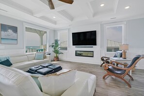 A spacious living room with a white sofa, a flat-screen TV mounted above a fireplace, and a wooden rocking chair.