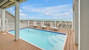 En pool med ett trädäck, vita solstolar och utsikt över havet.