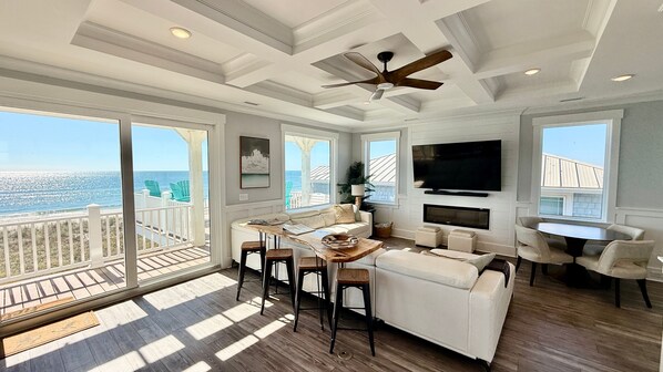 A spacious living room with a large TV, comfortable seating, and a balcony with a view of the ocean.