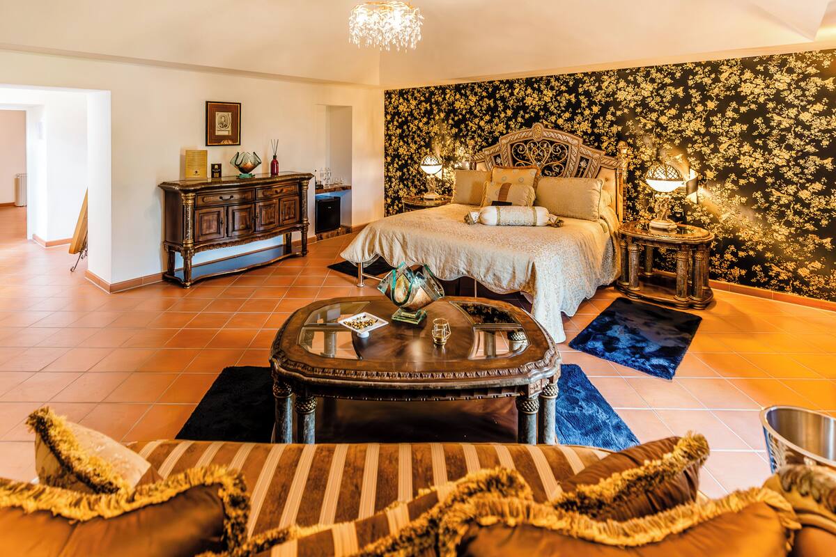 Une chambre à coucher avec un grand lit, une commode en bois, une table basse ronde et un lustre.