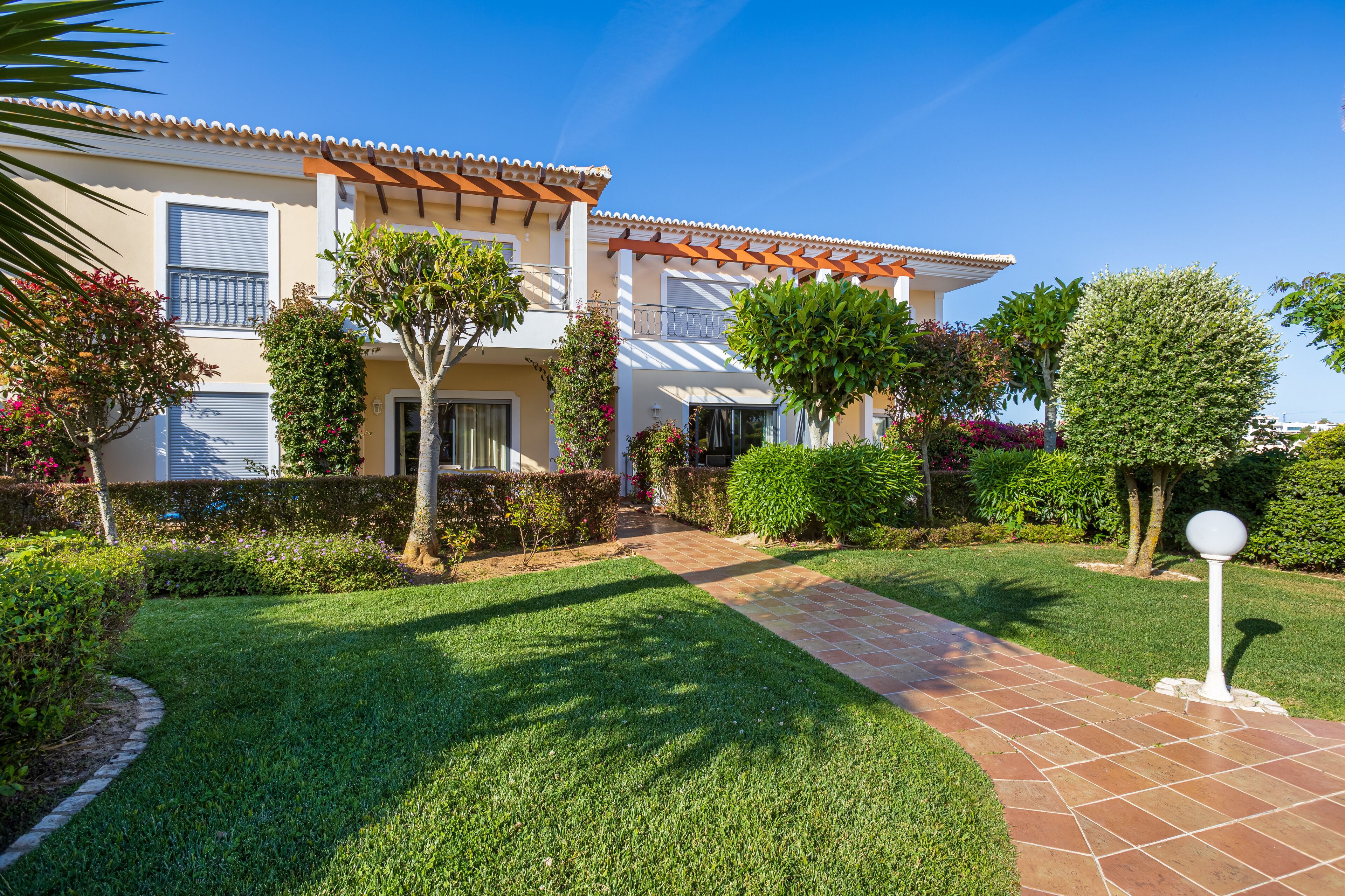 A house with a tiled roof, a paved pathway, and well-maintained gardens.