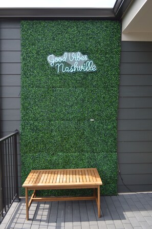 A wooden bench in front of a wall with a green wall and a neon sign that reads "Good Vibes Nashville".