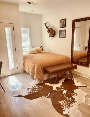 A bedroom with a bed, a bench, a cowhide rug, and a mirror.