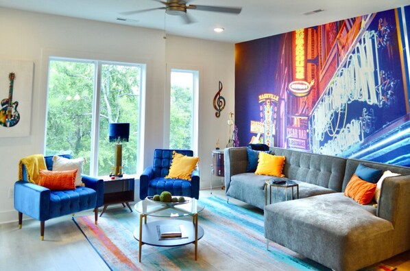A modern living room with a large window, a blue armchair, a grey sofa, and a colorful rug.