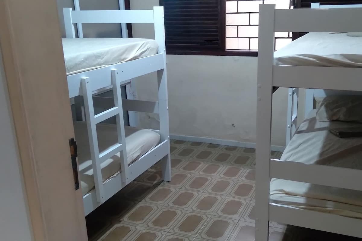 A room with bunk beds, a window with blinds, and patterned flooring.