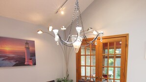 Un comedor con una mesa grande, seis sillas, una araña y un cuadro de un faro en la pared.