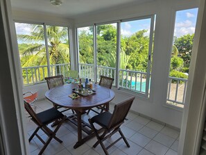 Une pièce baignée de lumière, avec une table ronde, des chaises et une vue sur une piscine et la verdure environnante.