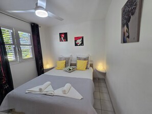 A hotel room with a bed, two bedside tables with lamps, a ceiling fan, and two windows with curtains.