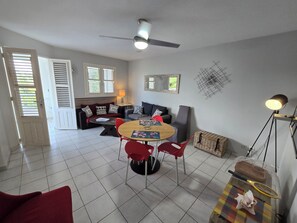 A living room with a dining table, red chairs, a ceiling fan, and a large window with blinds.