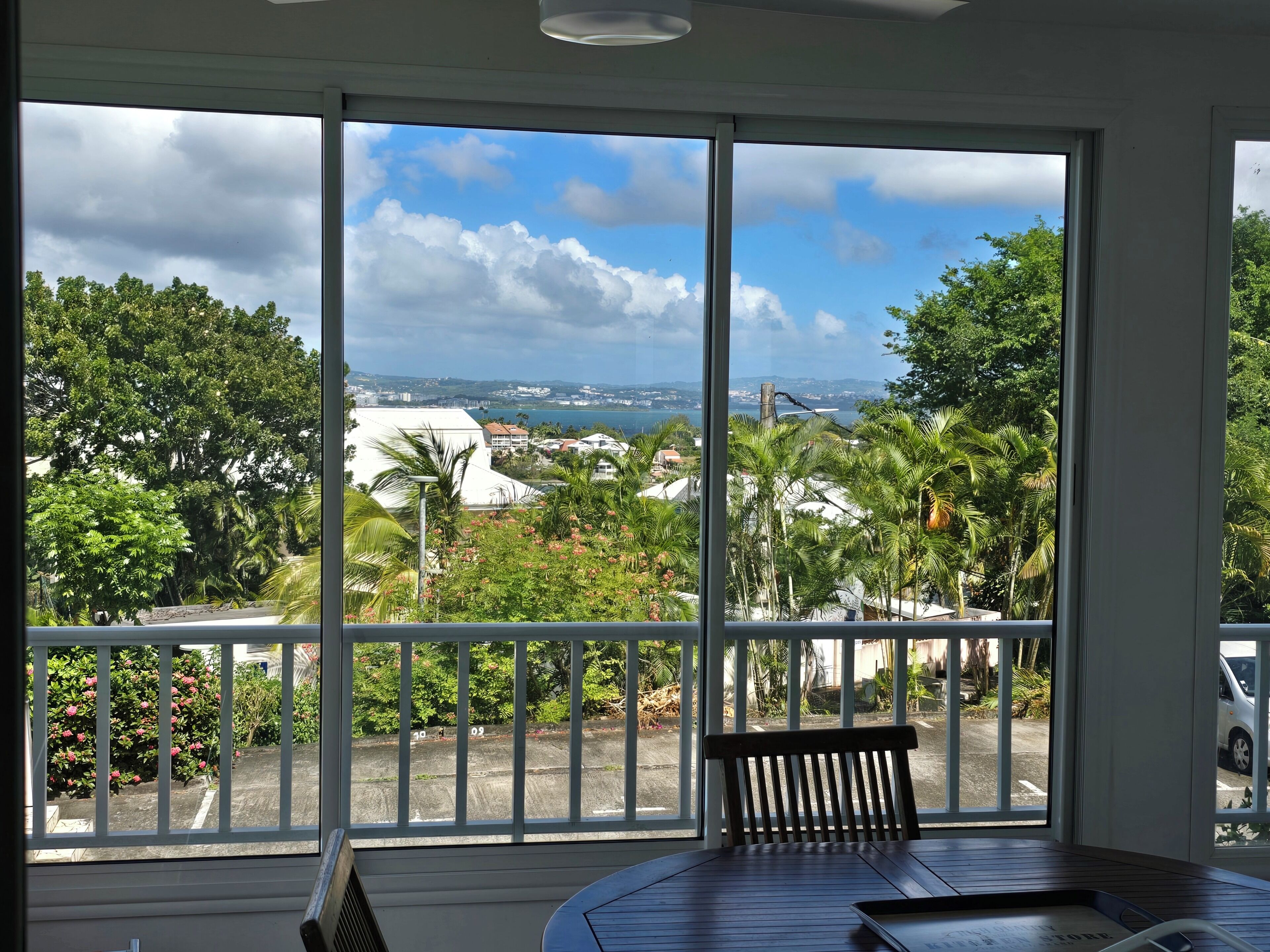 A room with a large window offering a view of a coastal area, a wooden table, and a chair.