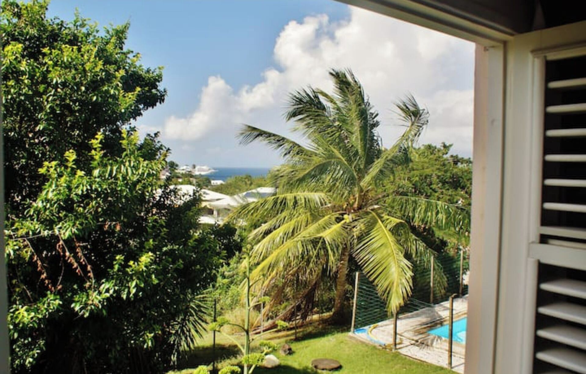 A view from a balcony overlooking a pool area with palm trees and a clear sky.