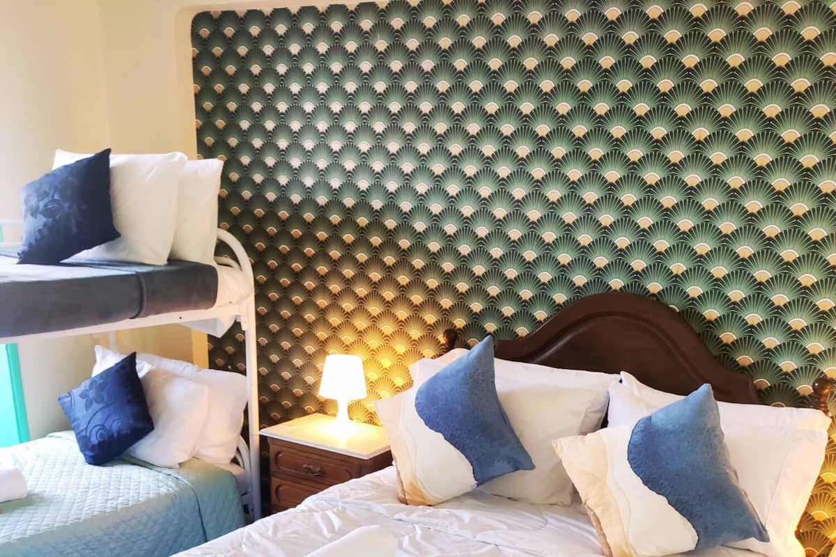 A hotel room with a bunk bed, a single bed, and a nightstand with a lamp.