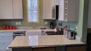 A kitchen with granite countertops, white cabinets, a microwave, and a gas stove. There are two bar stools and a window with a view of trees. -  2 bd 2bth, Thomas, WV, near Canaan and Davis, WV skiing, trails, State Parks  (Thomas)