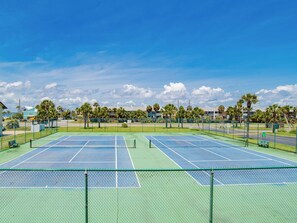 Ein Tennisplatz mit zwei Spielfeldern, umgeben von einem Zaun, und Palmen im Hintergrund.