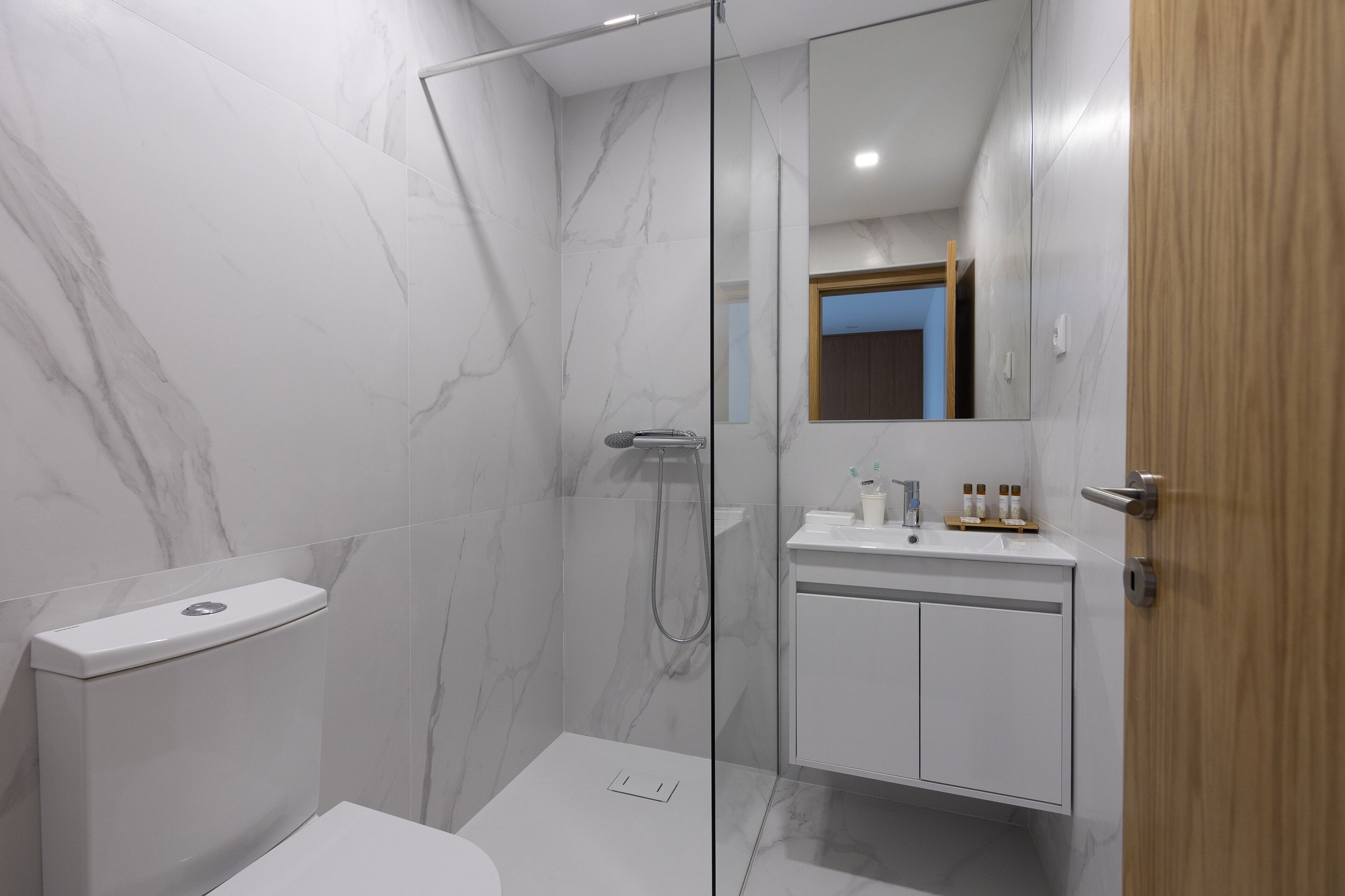 A modern bathroom with a glass shower enclosure, a white toilet, and a wooden door.