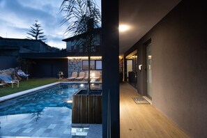A modern outdoor pool area with a stone wall, wooden deck, and lounge chairs. - Abraços dos Avós - Casas de Aldeia  (Viana do Castelo)
