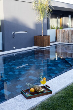 A swimming pool with a tiled deck, a wooden planter, and a tray with fruits and a drink. - Abraços dos Avós - Casas de Aldeia  (Viana do Castelo)