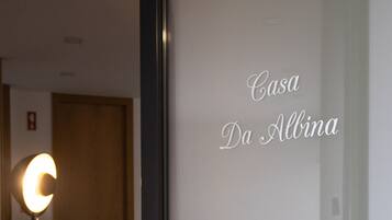 Habitació d'hotel amb un llit, una petita taula de nit i una làmpada. La habitació té una porta amb un panell de vidre mossegat que mostra el text "Casa Da Albina".