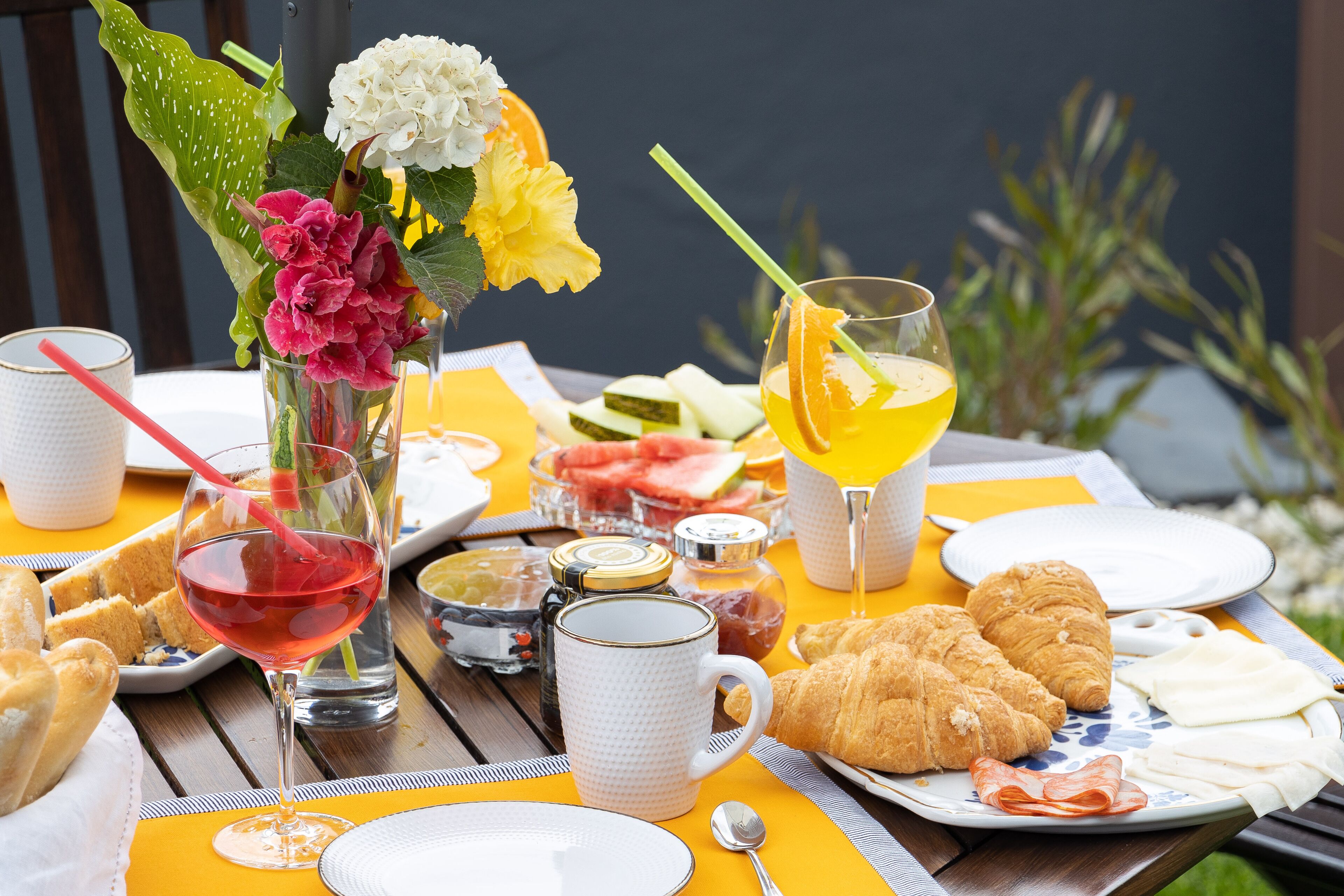 Una mesa de desayuno con croissants, jugo de naranja y un florero con flores.