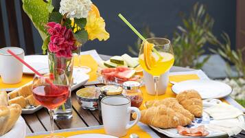 Una mesa de desayuno con croissants, jugo de naranja y un florero con flores.