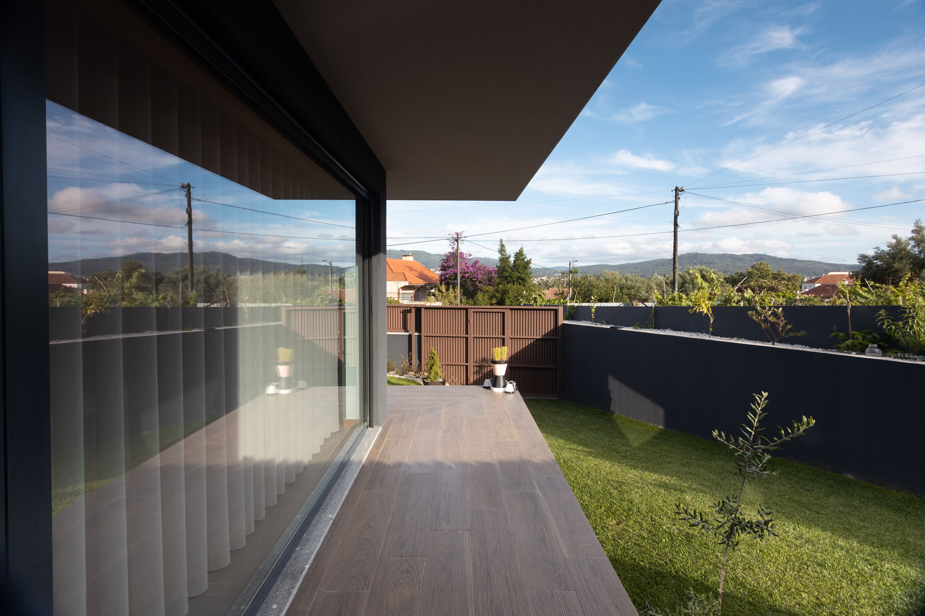 A modern building with a glass facade, a wooden deck, and a view of a garden and distant mountains.
