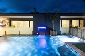 A modern outdoor pool area with a blue-lit water feature, stone walls, and potted plants. - Abraços dos Avós - Casas de Aldeia  (Viana do Castelo)