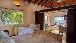 Een slaapkamer met twee bedden, een houten plafond, een groot raam en een balkon met uitzicht op zee.