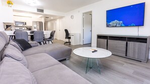 Una sala de estar moderna con un sofá seccional gris, una mesa de vidrio redonda y un televisor de pantalla plana montado en la pared.