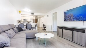 Una sala de estar moderna con un sofá gris, una mesa de centro de vidrio y una cocina al fondo.