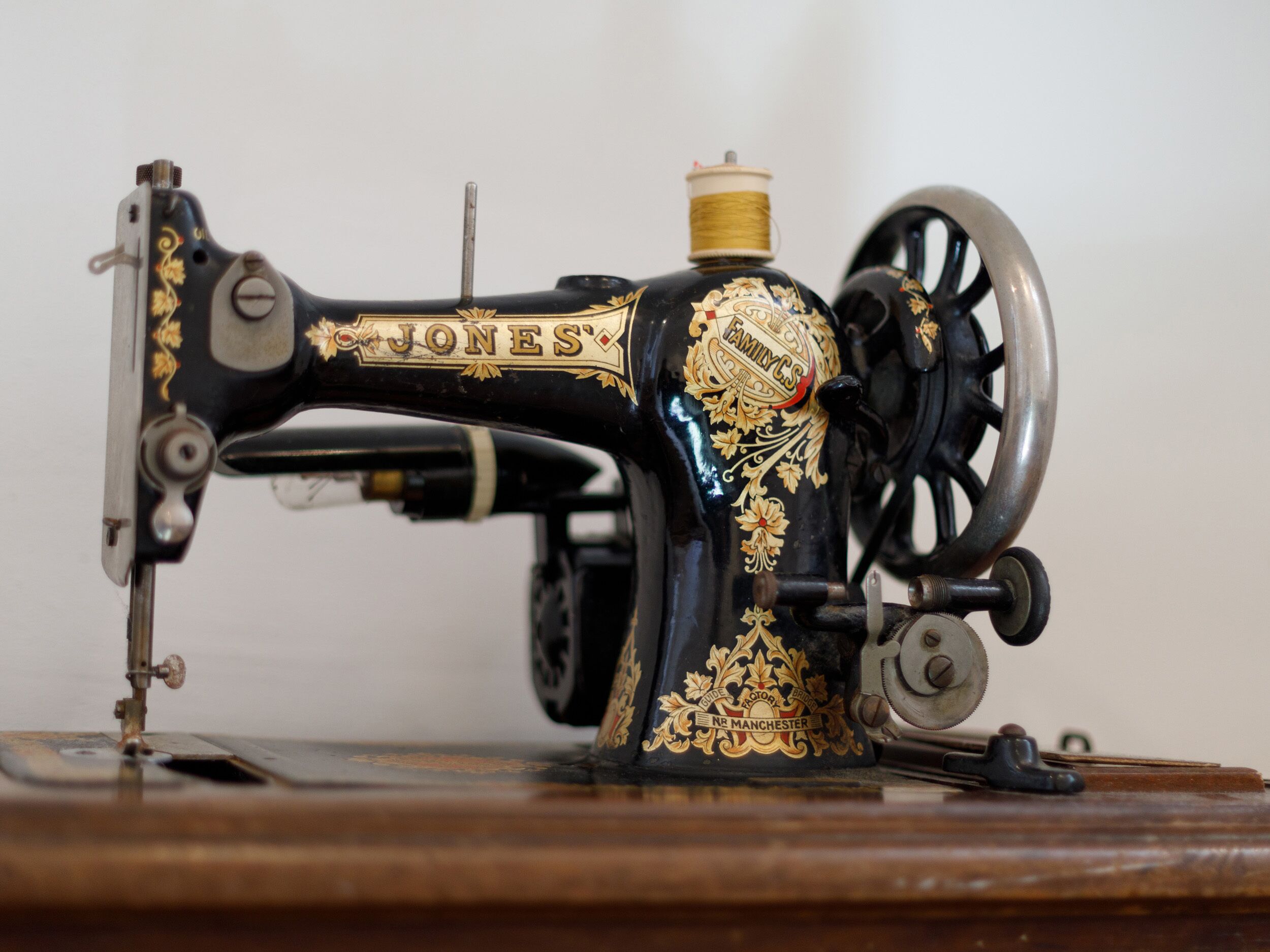 Una máquina de coser antigua con detalles dorados decorativos y el nombre de marca 'JONES' a la vista.