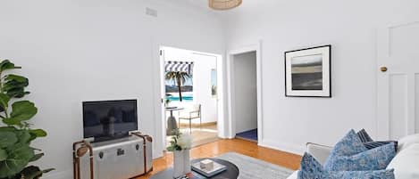 Una sala de estar moderna con un sofá, una mesa de centro, un televisor sobre un mueble bajo y una planta grande.