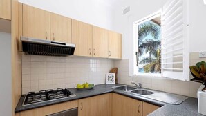 A kitchen with wooden cabinets, a gas stove, a sink, and a window with blinds. - Absolute Seafront Bronte (Bronte)
