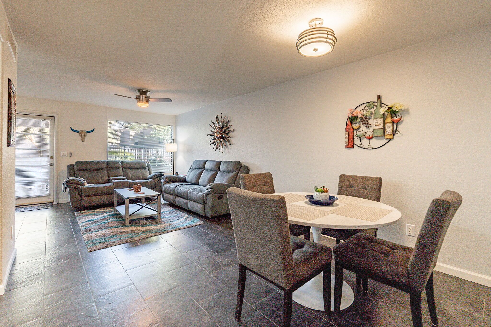 A living room with a gray sectional sofa, a coffee table, and a dining area with a round table and chairs.