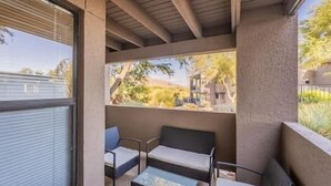 A covered outdoor seating area with a sofa and two chairs, a small table, and a view of a residential area with trees and houses. - Spacious Split Floor Plan with Pool and Mountain views (Tucson)