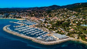 An aerial view of a coastal town with a marina, residential buildings, and hills in the background.