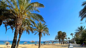 A beach with palm trees, umbrellas, and a clear blue sky.