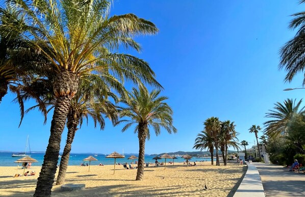 A beach with palm trees, umbrellas, and a clear blue sky. - Beautiful studio with airco cabin 4pers view and sea front. 
WIFI and Parking (Le Lavandou)