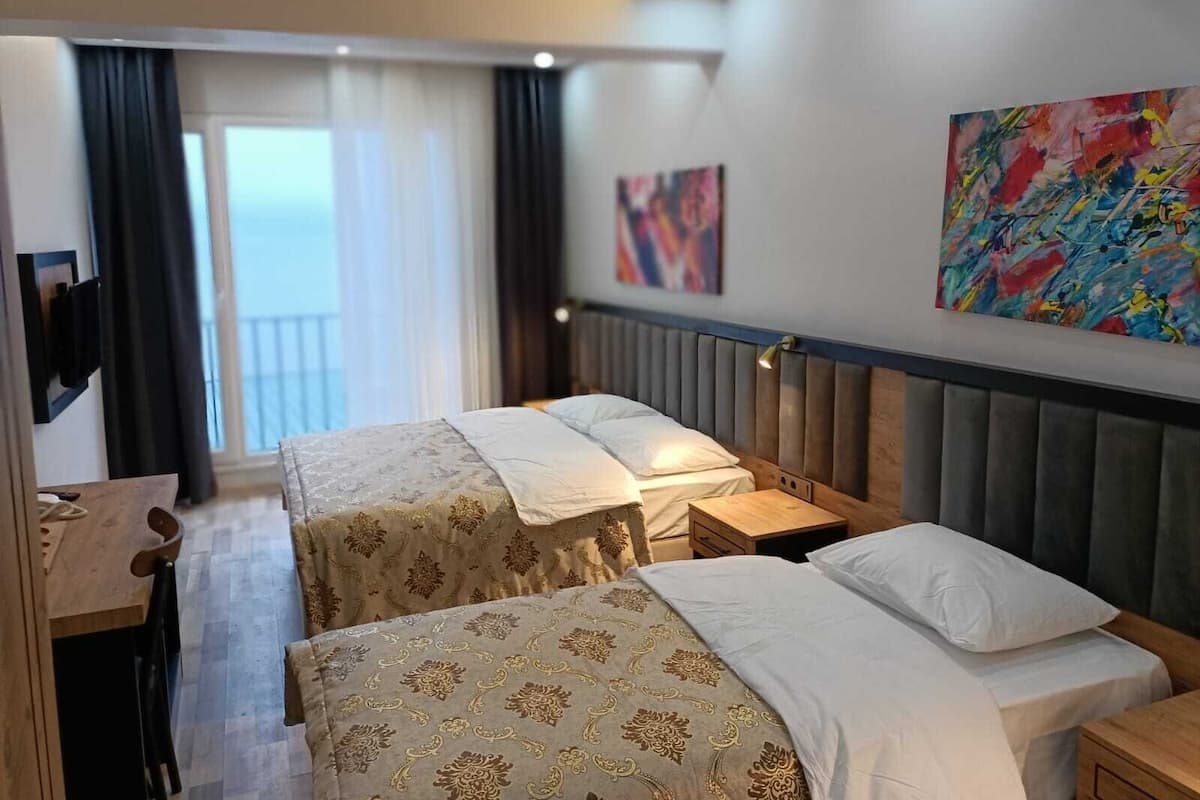 A hotel room with two beds, a desk, and a view of the sea.