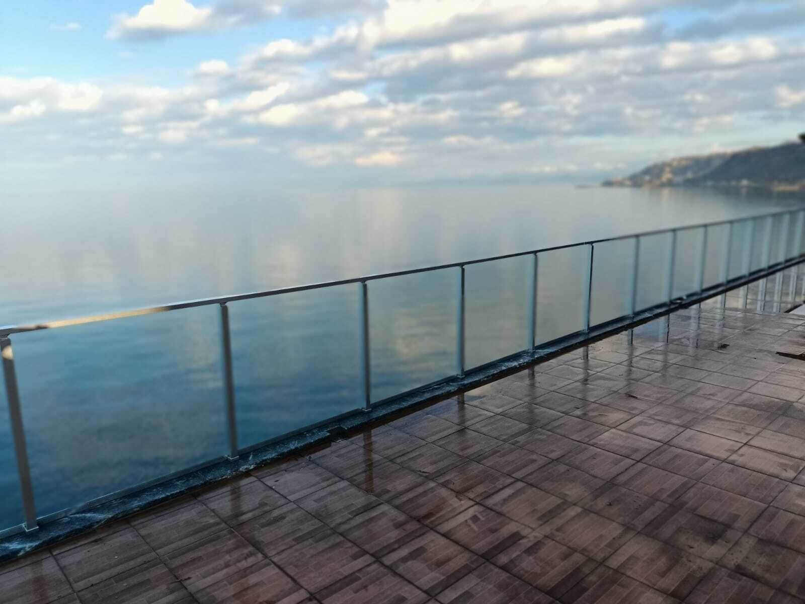 A waterfront promenade with a glass railing and tiled flooring.