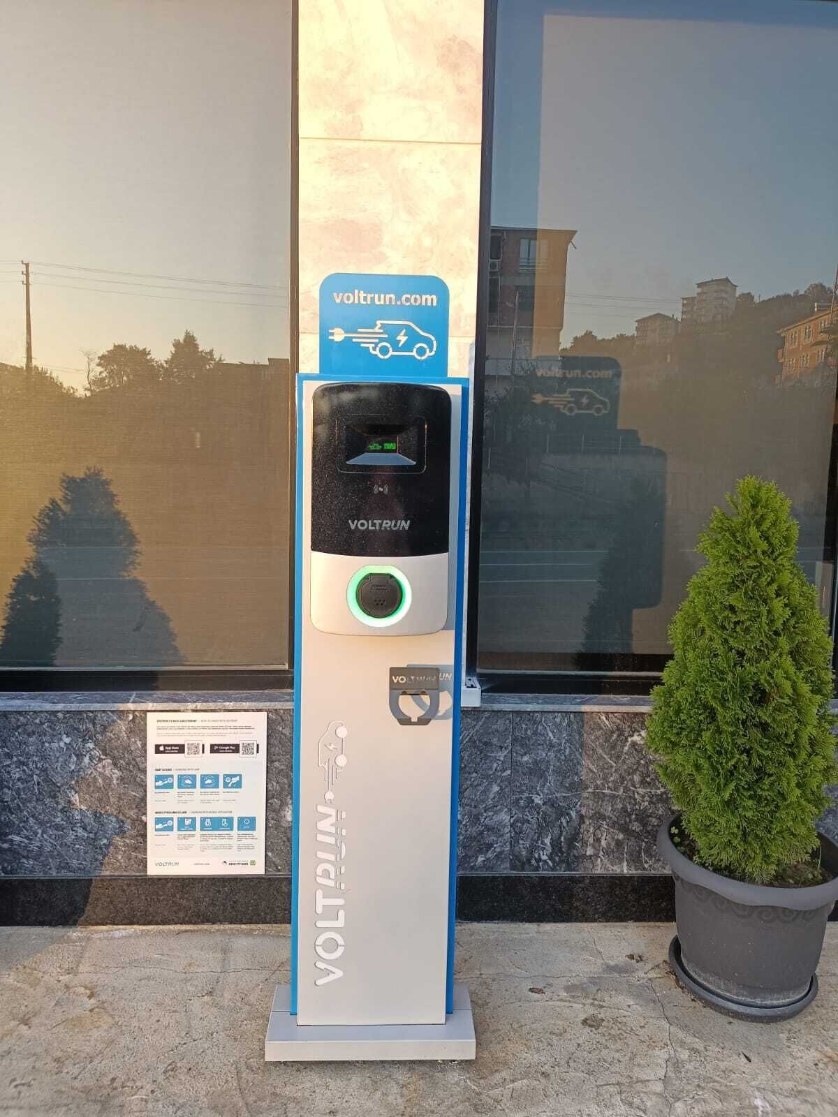 Une borne de recharge pour véhicules électriques VOLTRUN dotée d’un écran numérique, d’un indicateur de charge et d’un code QR pour accéder à des informations.