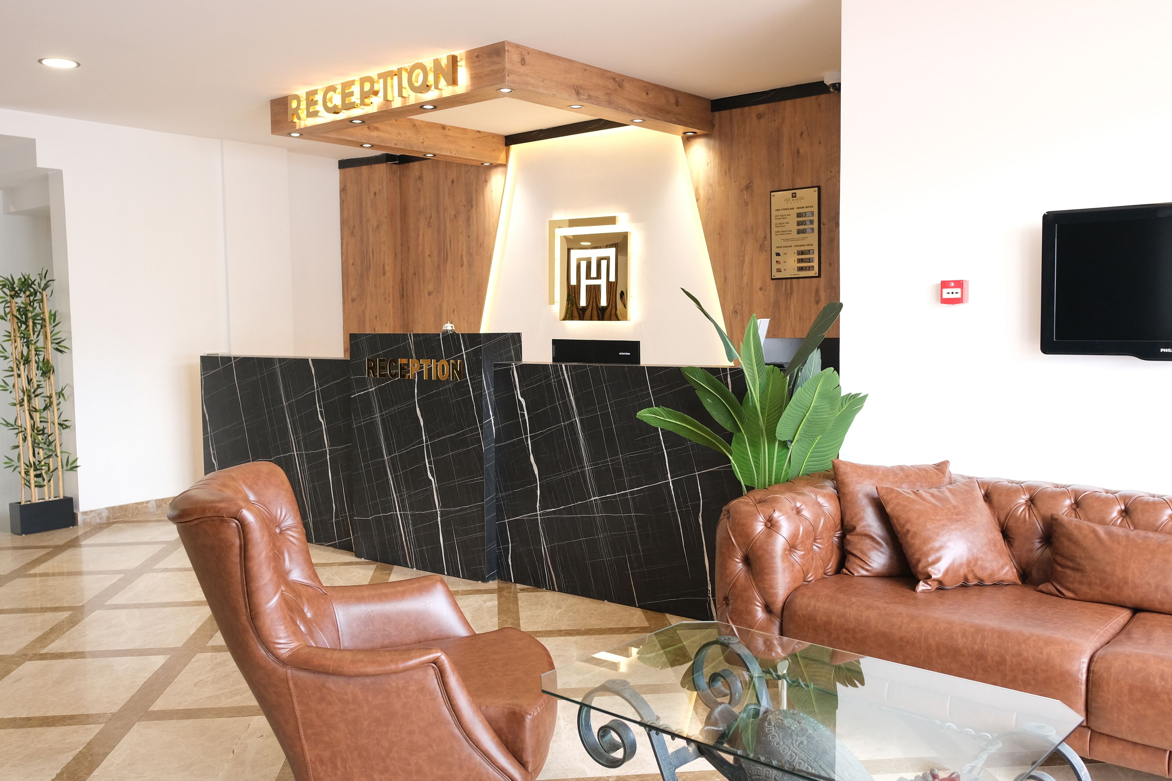 Zona de recepción con mostrador de madera, pared de mármol negro, sofá de cuero y mesa de centro de vidrio.