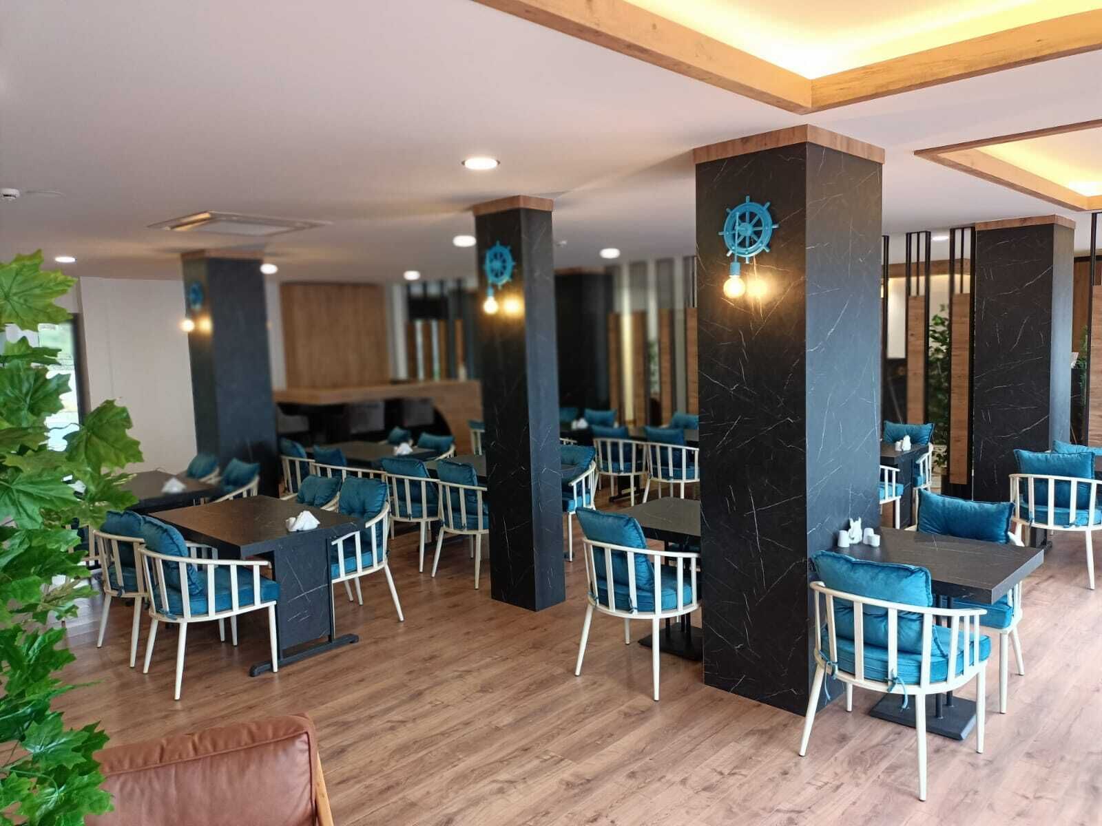 Um restaurante moderno com piso de madeira, cadeiras estofadas em azul e pilares de mármore preto.