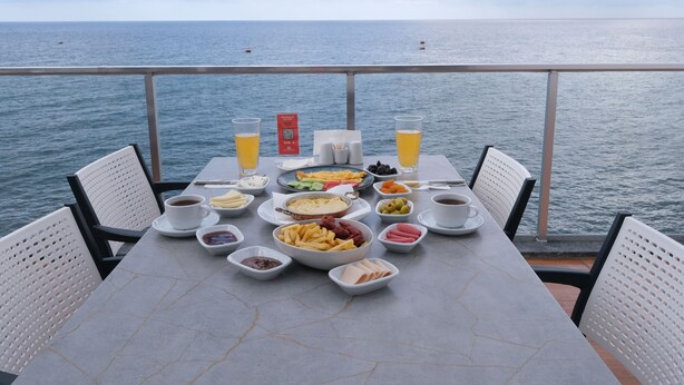 A table set with breakfast items and drinks, overlooking the sea. - The Marine Hotel  (Arsin)