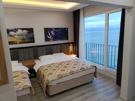 Un dormitorio con un ventanal amplio que ofrece vista al mar, una cama con colcha estampada y dos cuadros colgados en la pared.