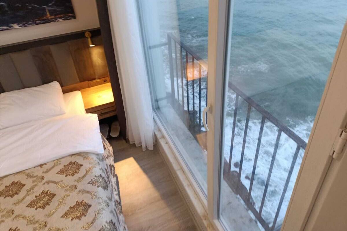 A hotel room with a bed, a nightstand, a window with a view of the sea, and a curtain.