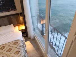 Habitación de hotel con cama, mesita de noche, ventana con vista al mar y cortina.