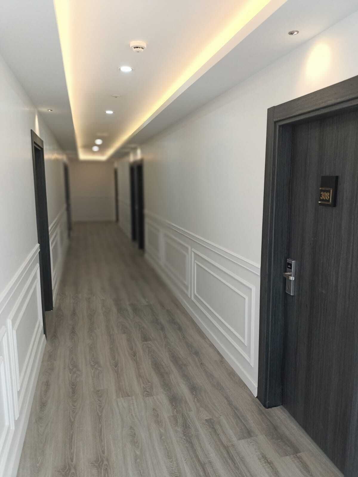 A hallway with a wooden floor, white wainscoting, and dark wooden doors.