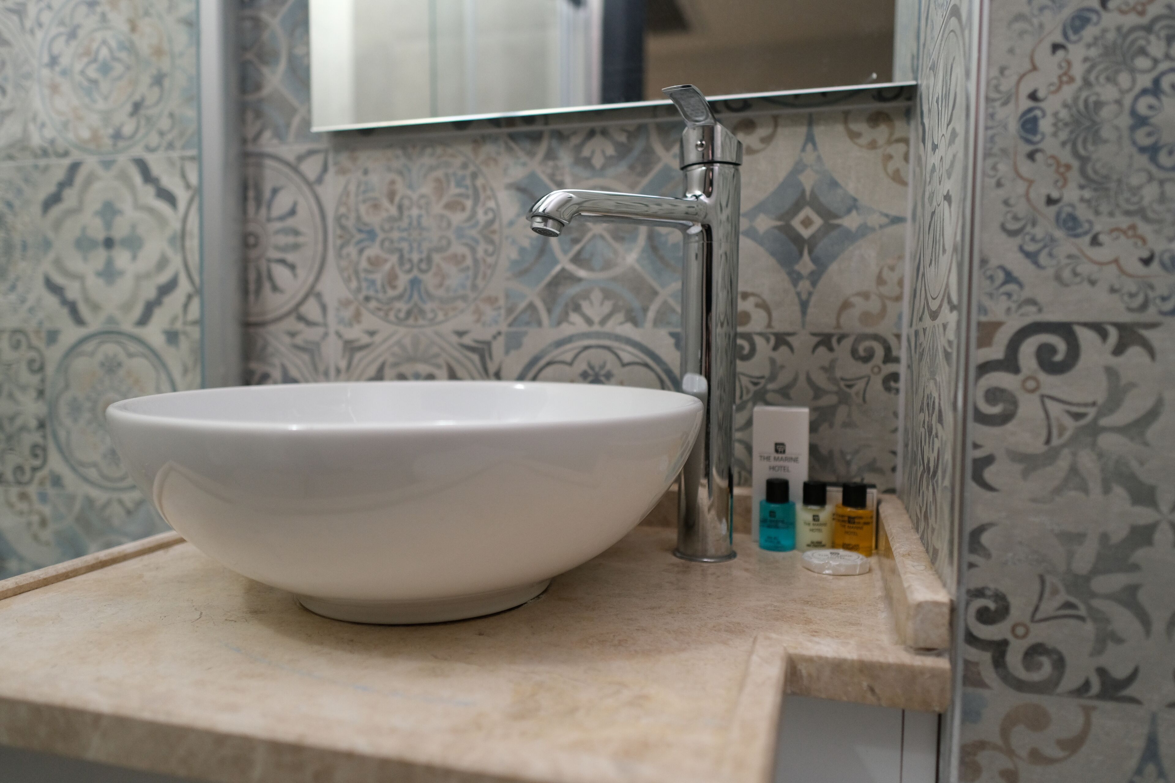 Un baño con un lavamanos blanco, un grifo moderno y azulejos decorativos en las paredes.