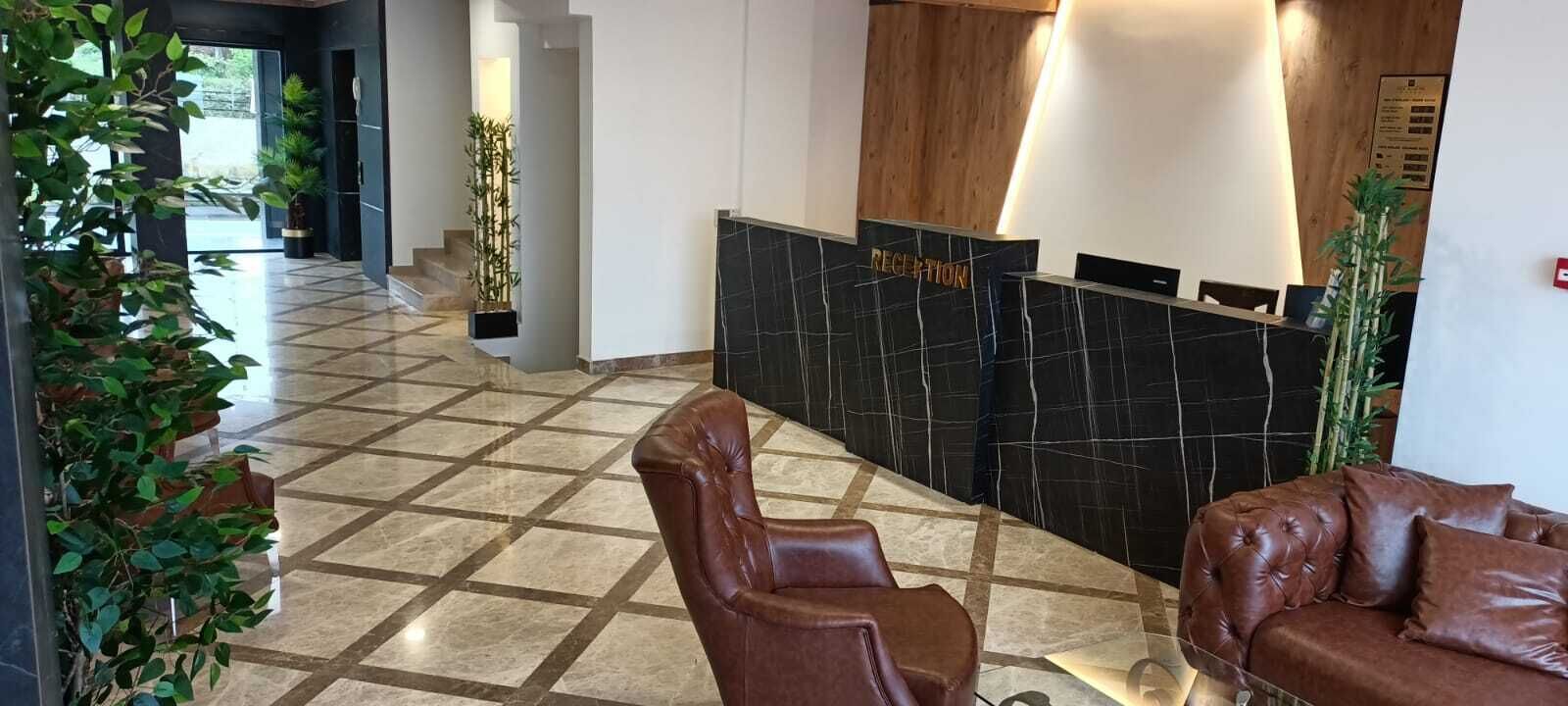 Uma área de recepção com balcão de check-in, um sofá de couro marrom e plantas em vasos.